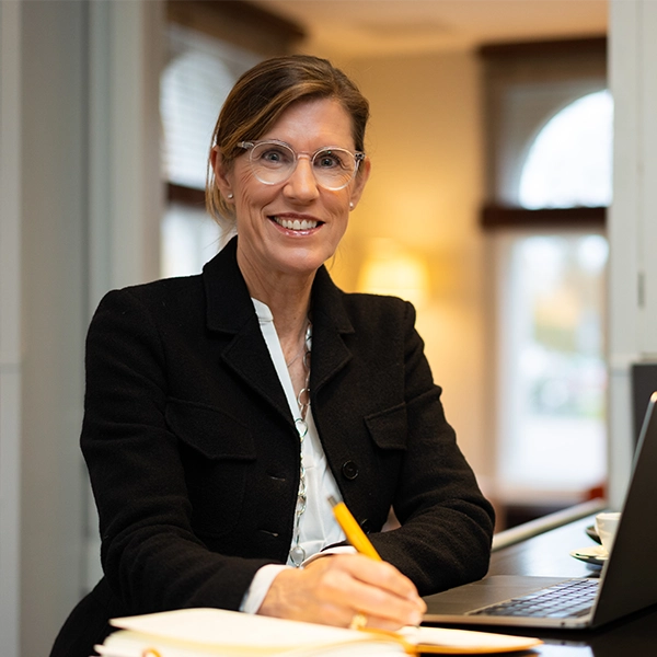 Maja Schneider von Smiling Customer lächelt am Schreibtisch und macht sich Notizen während ihrer Beratungsarbeit.