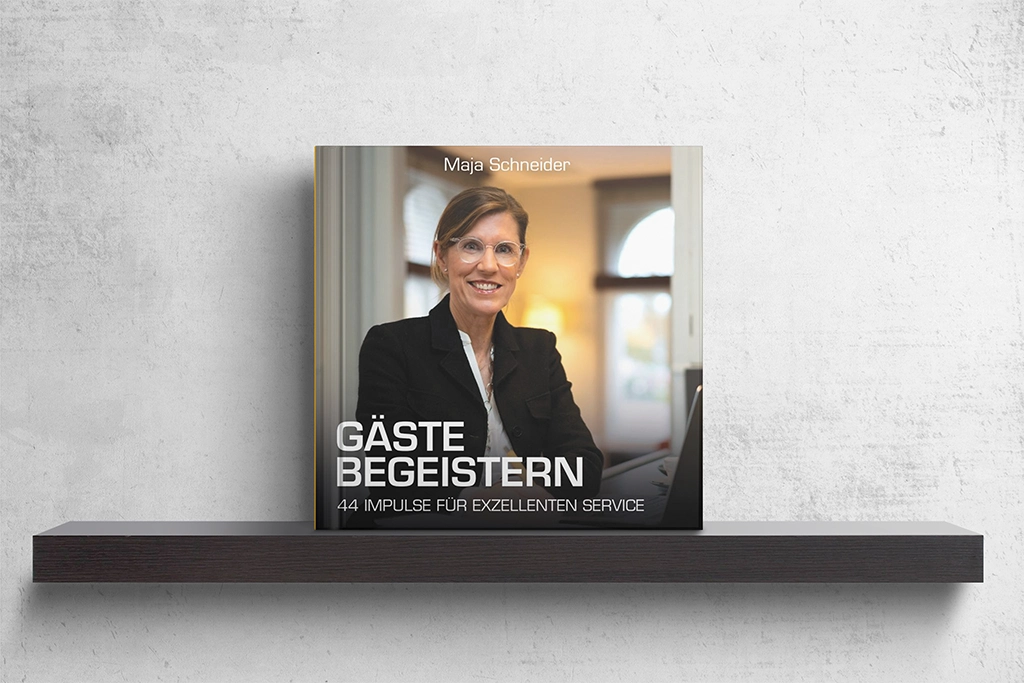 Buchcover ‚Gäste begeistern – 44 Impulse für exzellenten Service‘ von Maja Schneider auf einem Regal präsentiert.