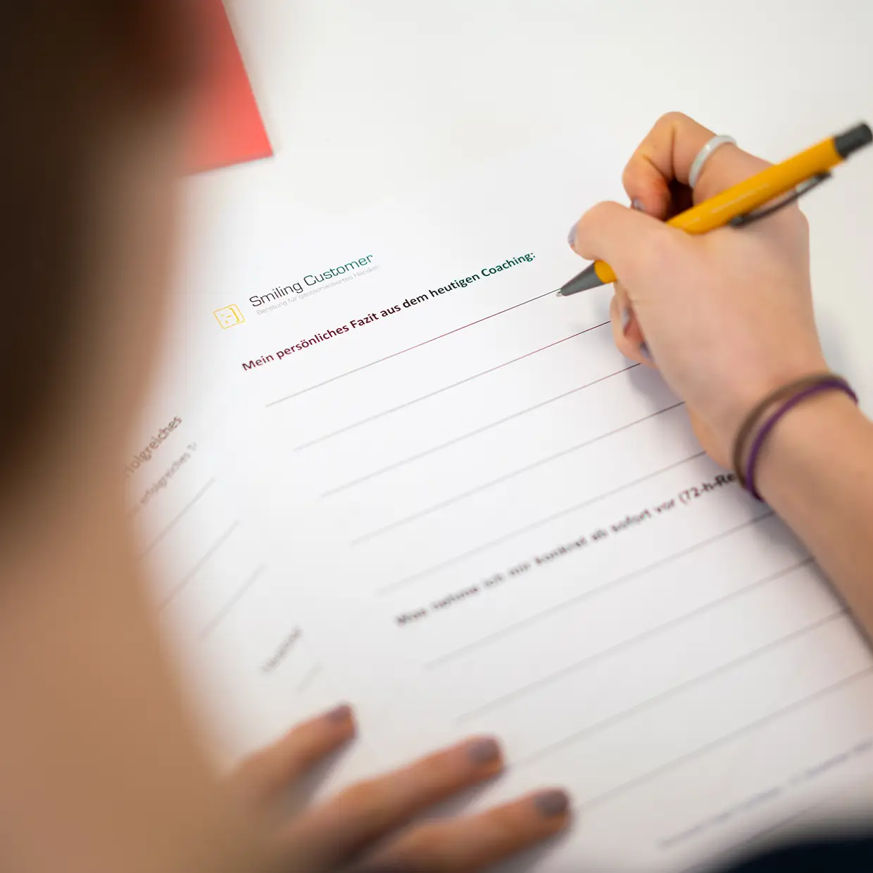 Teilnehmerin schreibt ihr persönliches Fazit in ein Coaching-Arbeitsblatt von Smiling Customer während eines Trainings.