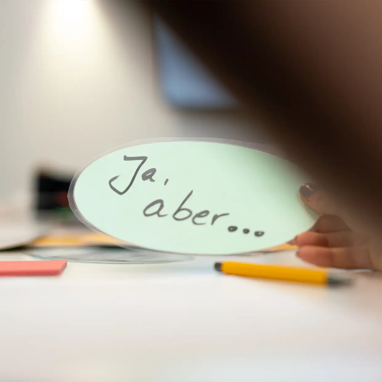 Hand hält Moderationskarte mit der Aufschrift ‚Ja, aber…‘ während eines Kommunikations- oder Service-Coachings