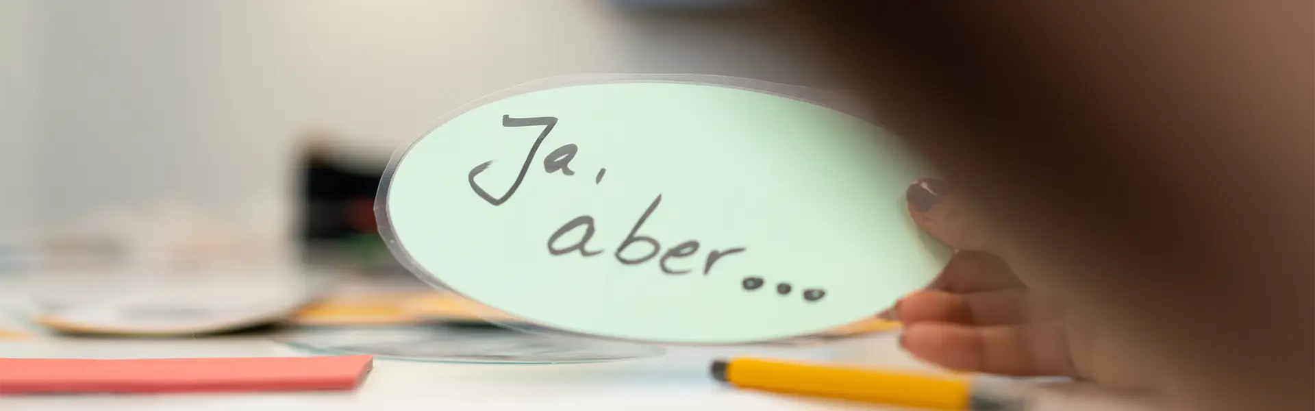 Hand hält Moderationskarte mit der Aufschrift ‚Ja, aber…‘ während eines Kommunikations- oder Service-Coachings.