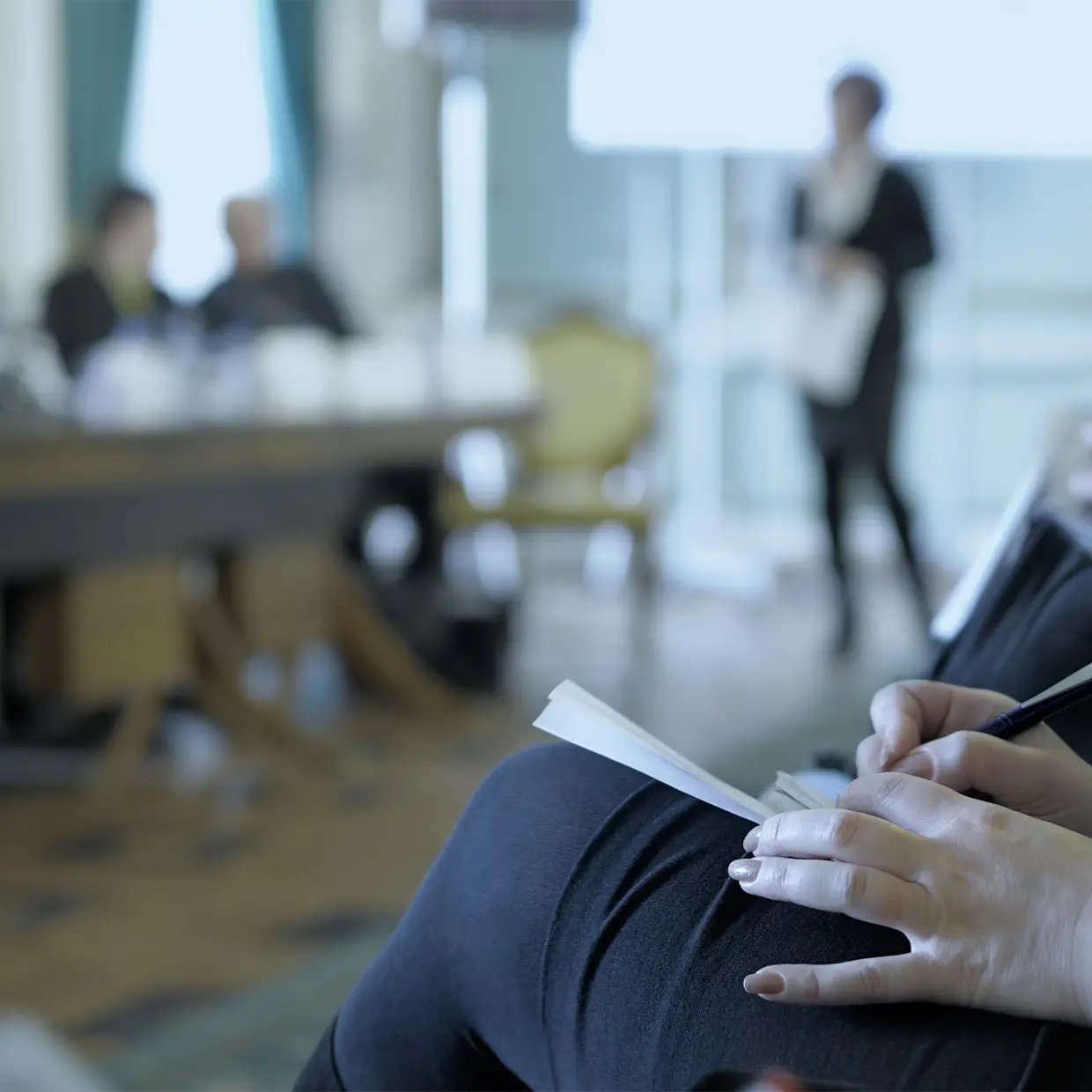 Teilnehmer eines Seminars machen sich Notizen, während eine Trainerin vorne präsentiert, im Rahmen einer professionellen Fortbildung für Führungskräfte.