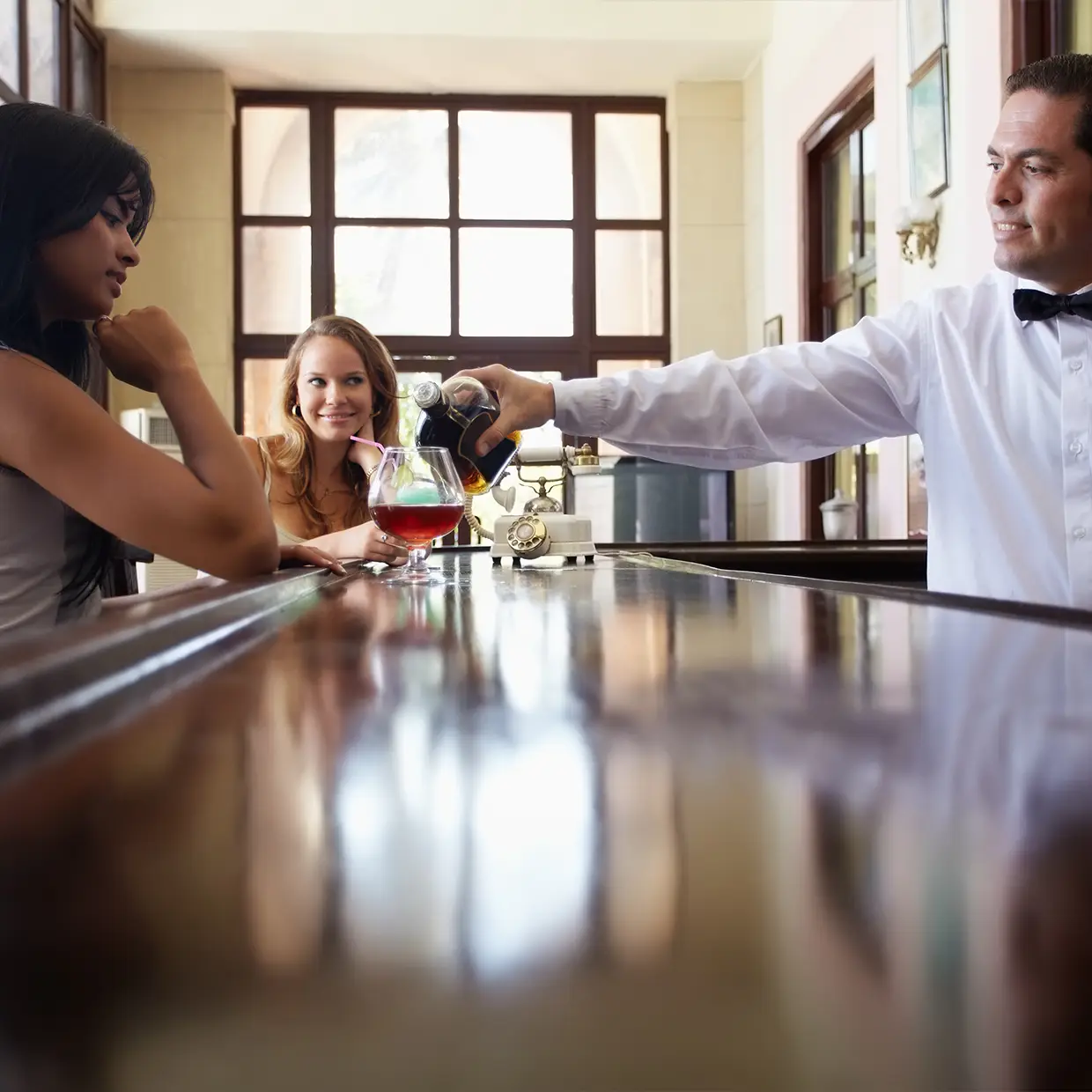 Barkeeper schenkt Gästen aufmerksam Getränke ein und zeigt serviceorientierte Kommunikation im Rahmen eines professionellen Service Trainings im Hotel.
