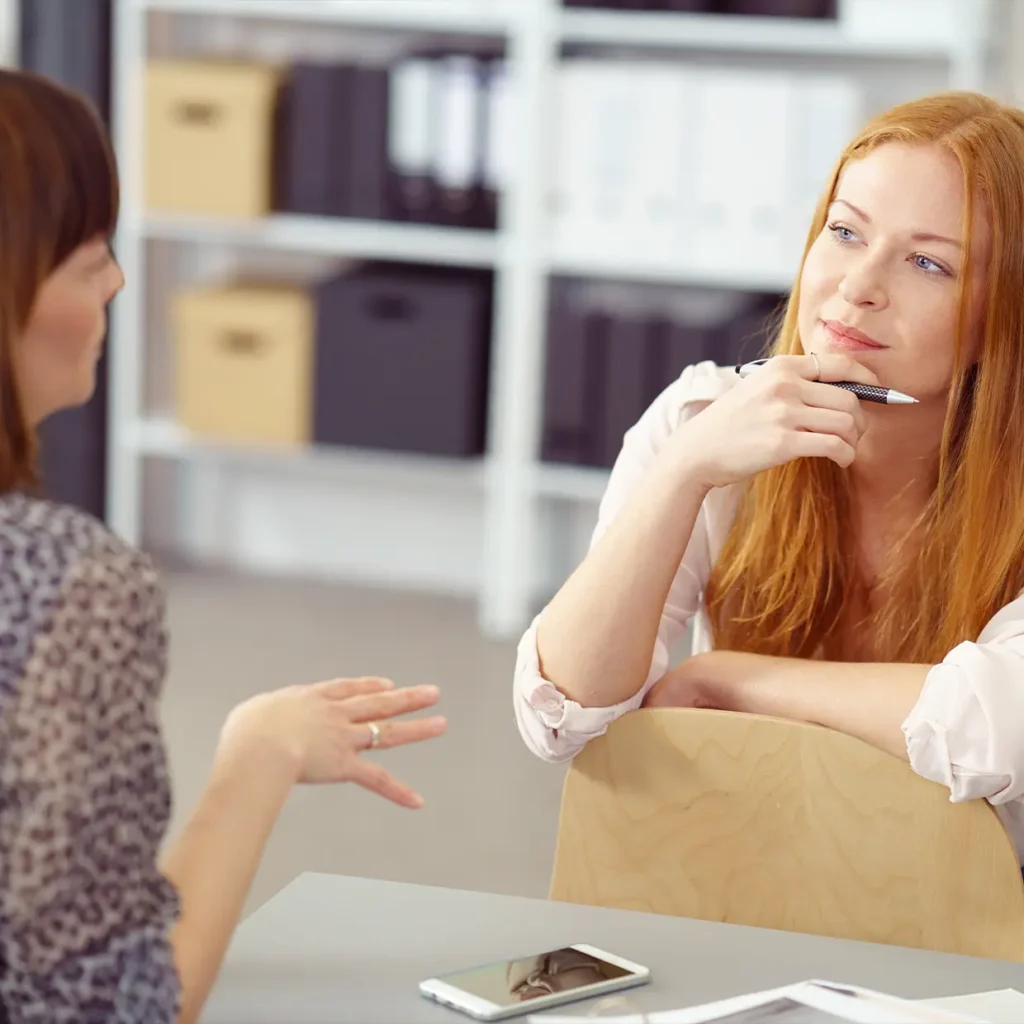 Führungskraft hört einer Mitarbeiterin aufmerksam zu und zeigt professionelle Gesprächsführung im Rahmen eines Coaching-Gesprächs mit Fokus auf aktives Zuhören.