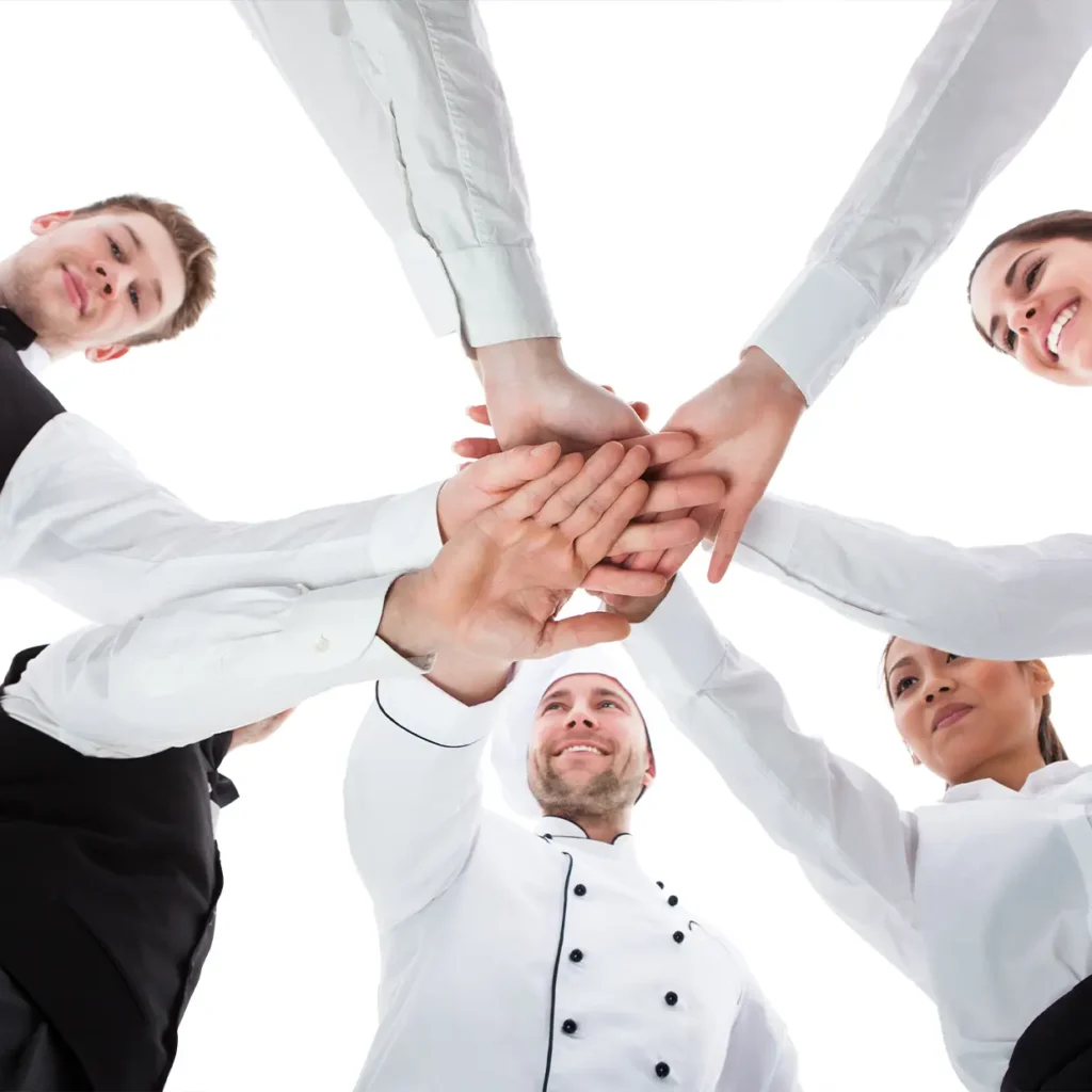 Hotelmitarbeiter in Uniform legen motiviert die Hände zusammen und zeigen starkes Teamwork im Rahmen eines professionellen Teambuilding Workshops.