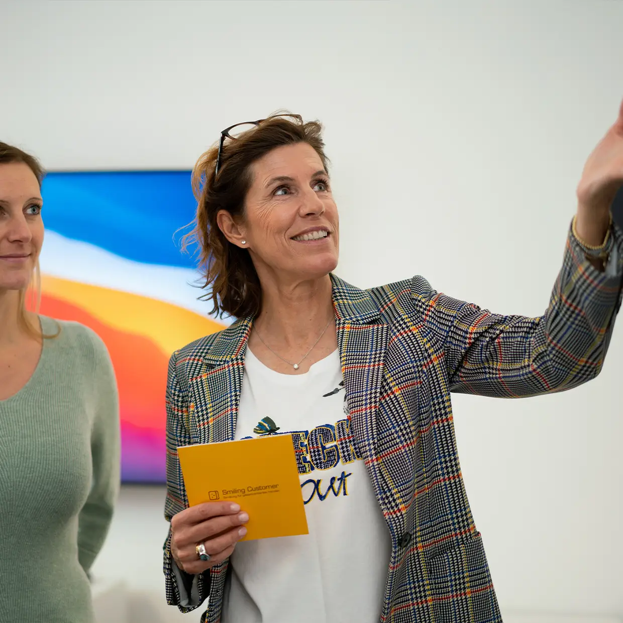 Maja Schneider von Smiling Customer erklärt Workshop-Inhalte und hält ein gelbes Moderationskärtchen, während sie gemeinsam mit Teilnehmenden über kundenorientierte Serviceideen spricht.